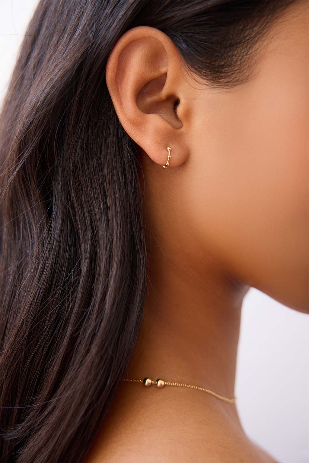 The Boules Gold Minibangle in 18k yellow gold, worn on the ear. Its three sculpted spheres rest lightly against the skin, drawing attention to the earlobe with quiet balance.