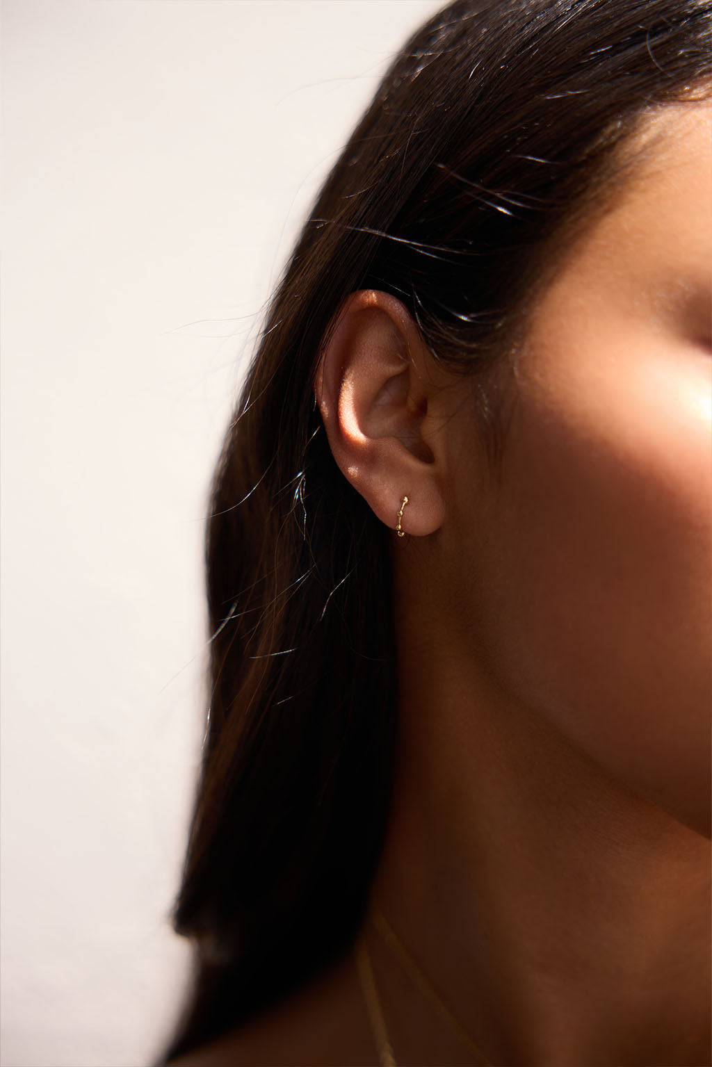 The Boules Gold Minibangle in 18k yellow gold, worn on the ear. Its three sculpted spheres rest lightly against the skin, drawing attention to the earlobe with quiet balance.