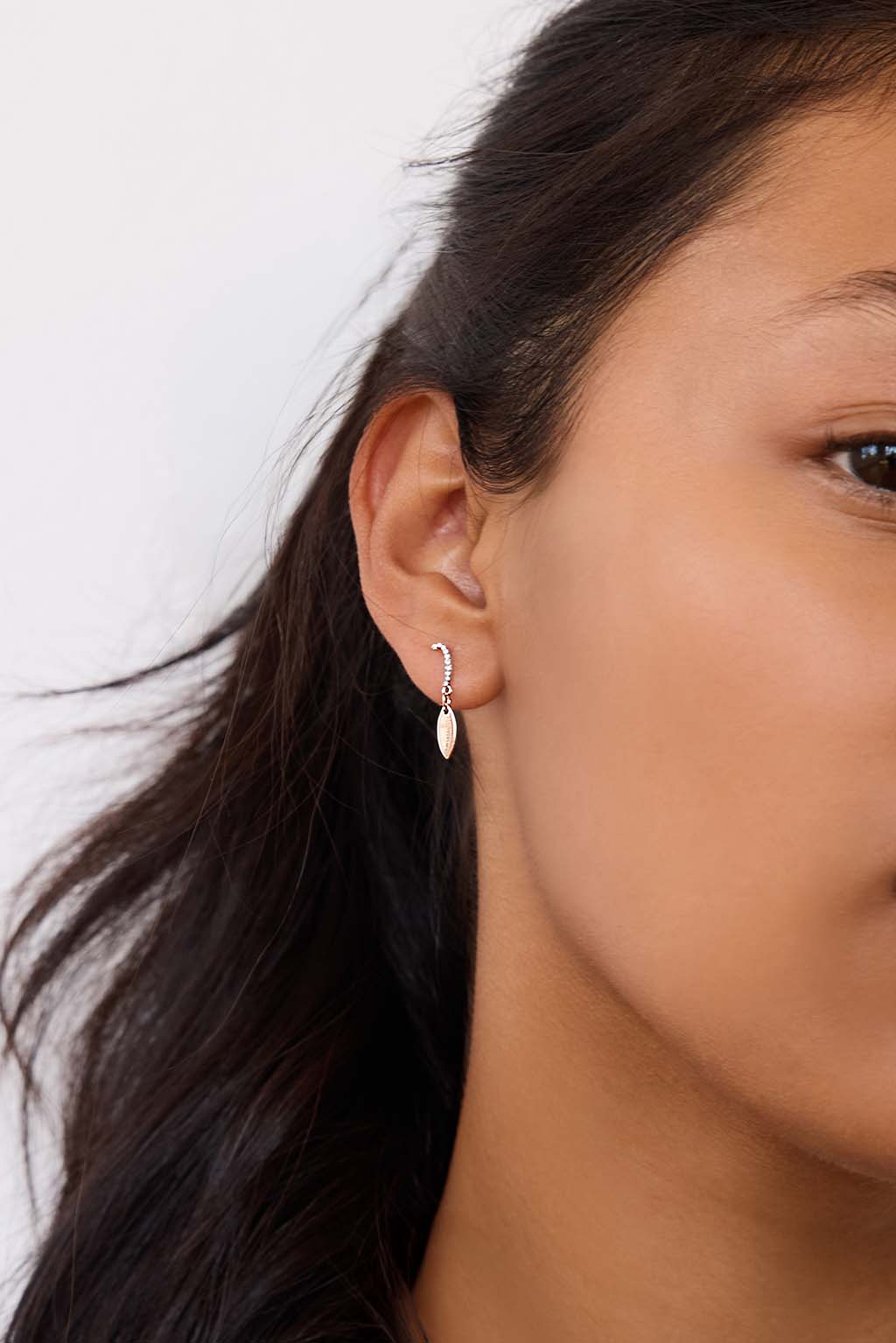 Model wearing the Little Feather earring in 18k gold. A delicate diamond element rests just below the earlobe, catching the light with subtle movement.