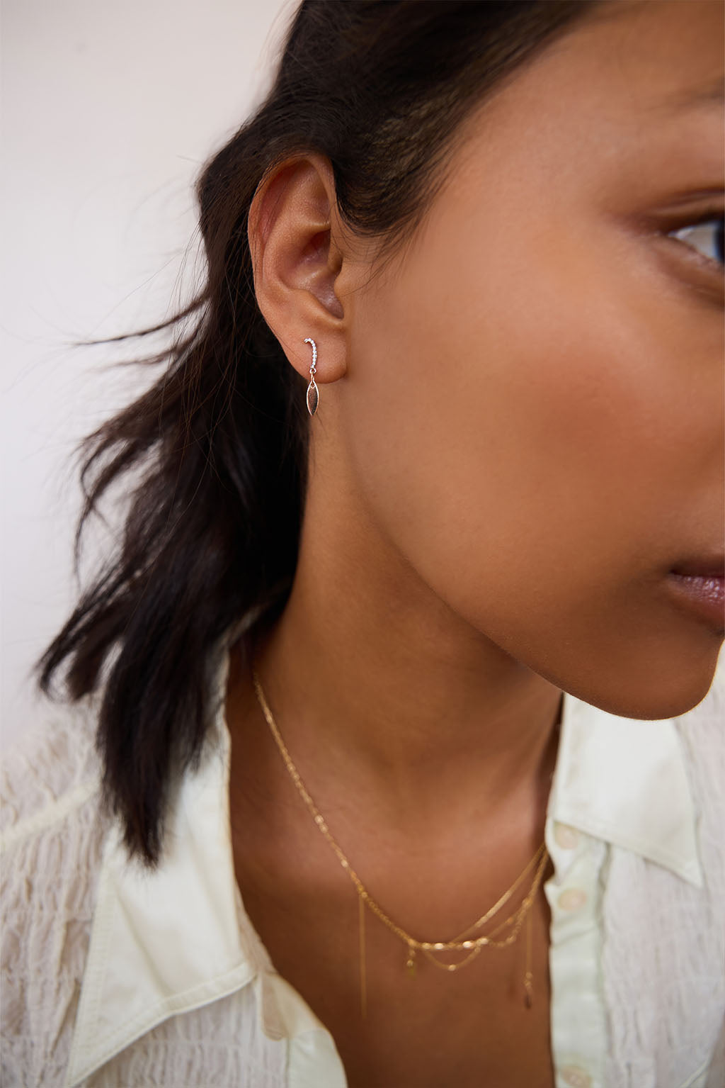 Model wearing the Little Feather earring in 18k gold. A delicate diamond element rests just below the earlobe, catching the light with subtle movement.