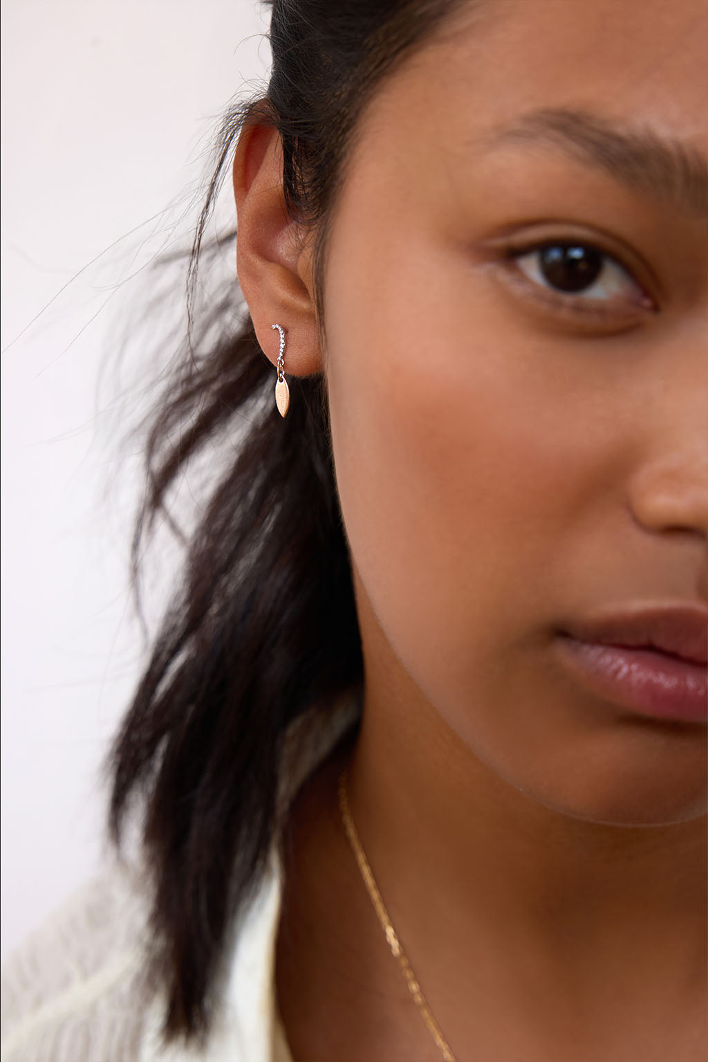 Model wearing the Little Feather earring in 18k gold. A delicate diamond element rests just below the earlobe, catching the light with subtle movement.