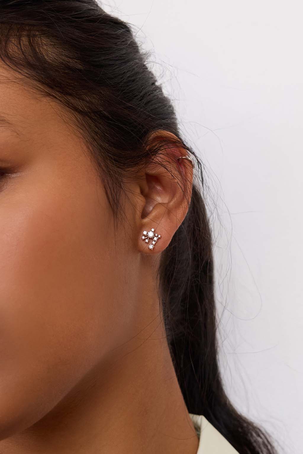 Model wearing the Star Cascade earring in 18k gold. A compact, asymmetrical cluster of diamonds sits close to the earlobe, catching the light like a suspended, luminous cascade. Delicate and easy to wear.