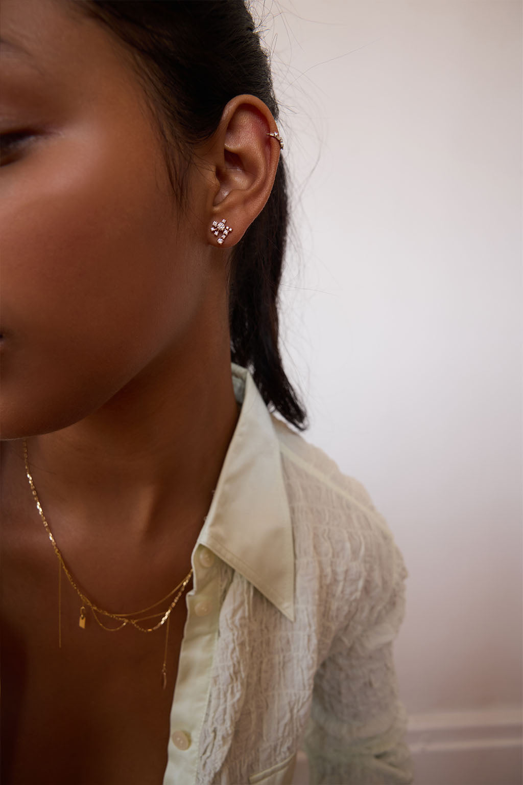 Model wearing the Star Cascade earring in 18k gold. A compact, asymmetrical cluster of diamonds sits close to the earlobe, catching the light like a suspended, luminous cascade. Delicate and easy to wear.