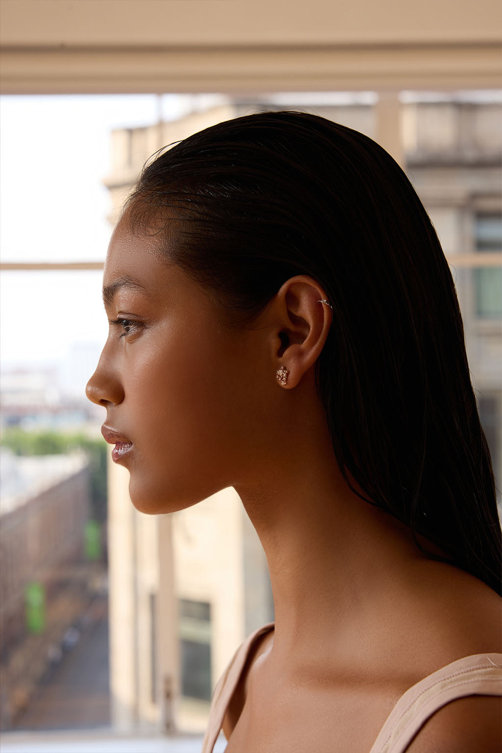 Model wearing the Star Cascade earring in 18k gold. A compact, asymmetrical cluster of diamonds sits close to the earlobe, catching the light like a suspended, luminous cascade. Delicate and easy to wear.