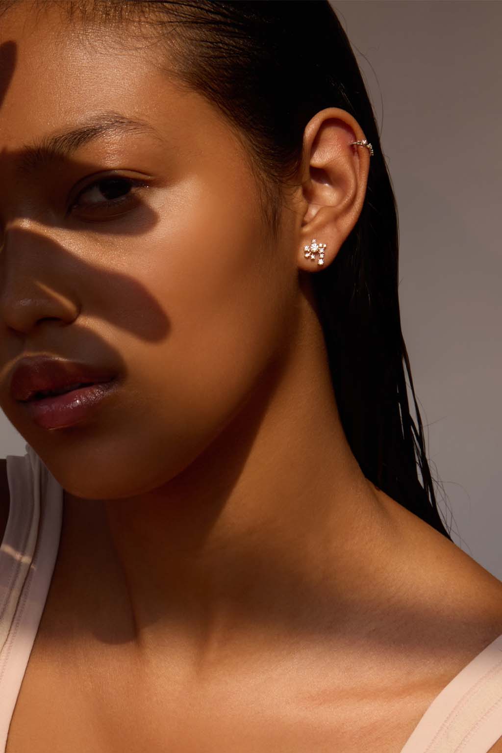Model wearing the Star Cascade earring in 18k gold. A compact, asymmetrical cluster of diamonds sits close to the earlobe, catching the light like a suspended, luminous cascade. Delicate and easy to wear.