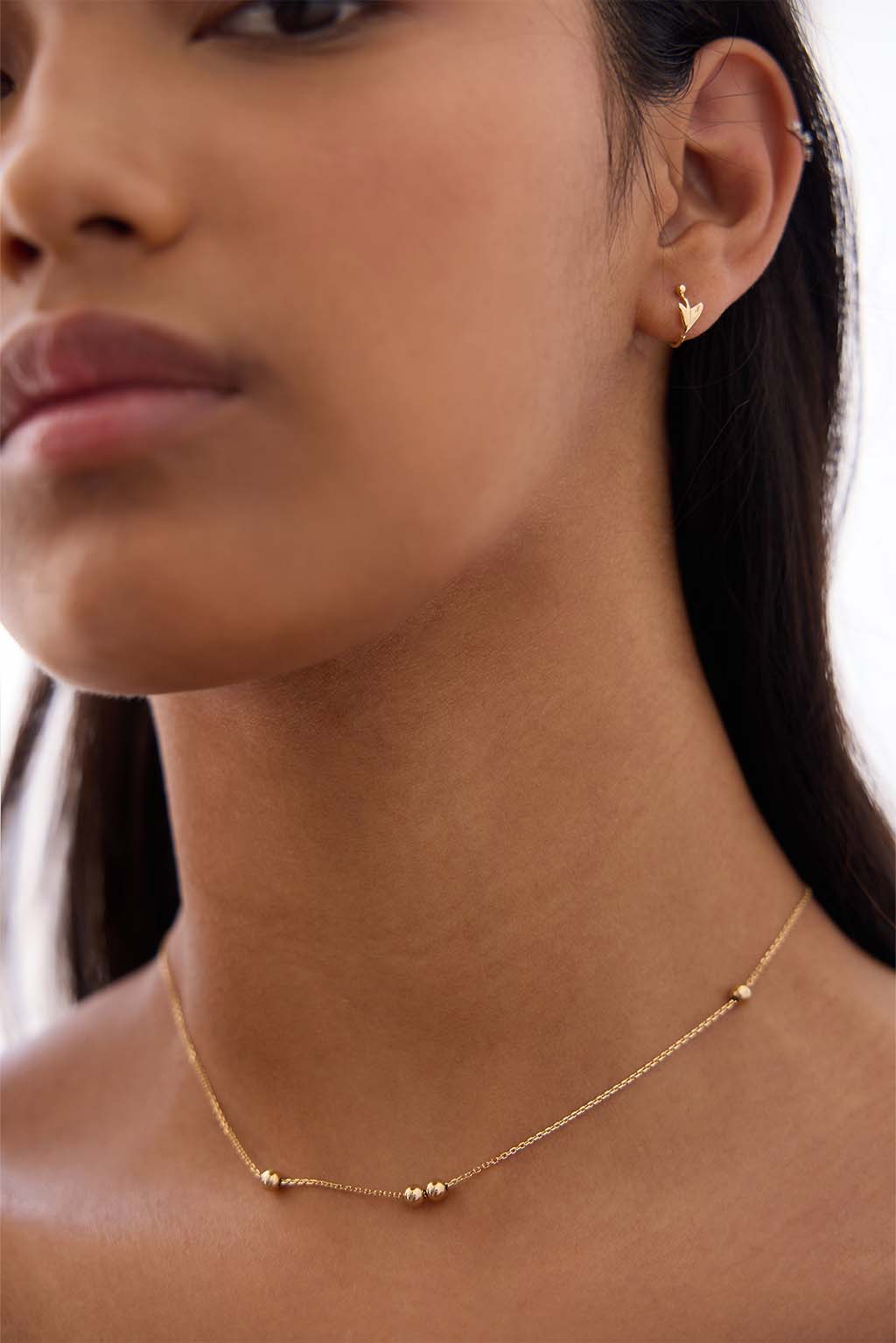 Worn close-up of the Floral Mini Bangle in 18k gold. The sculpted arrow and tiny sphere trace the curve of the ear in a soft, fluid gesture.