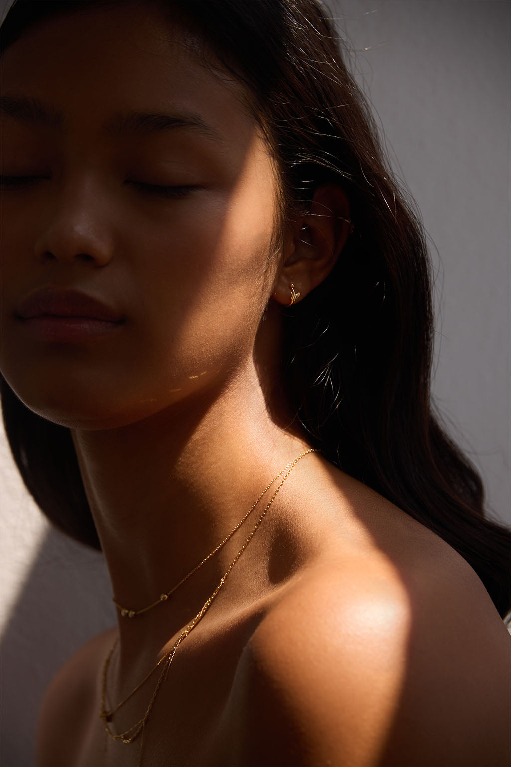 Worn close-up of the Floral Mini Bangle in 18k gold. The sculpted arrow and tiny sphere trace the curve of the ear in a soft, fluid gesture.