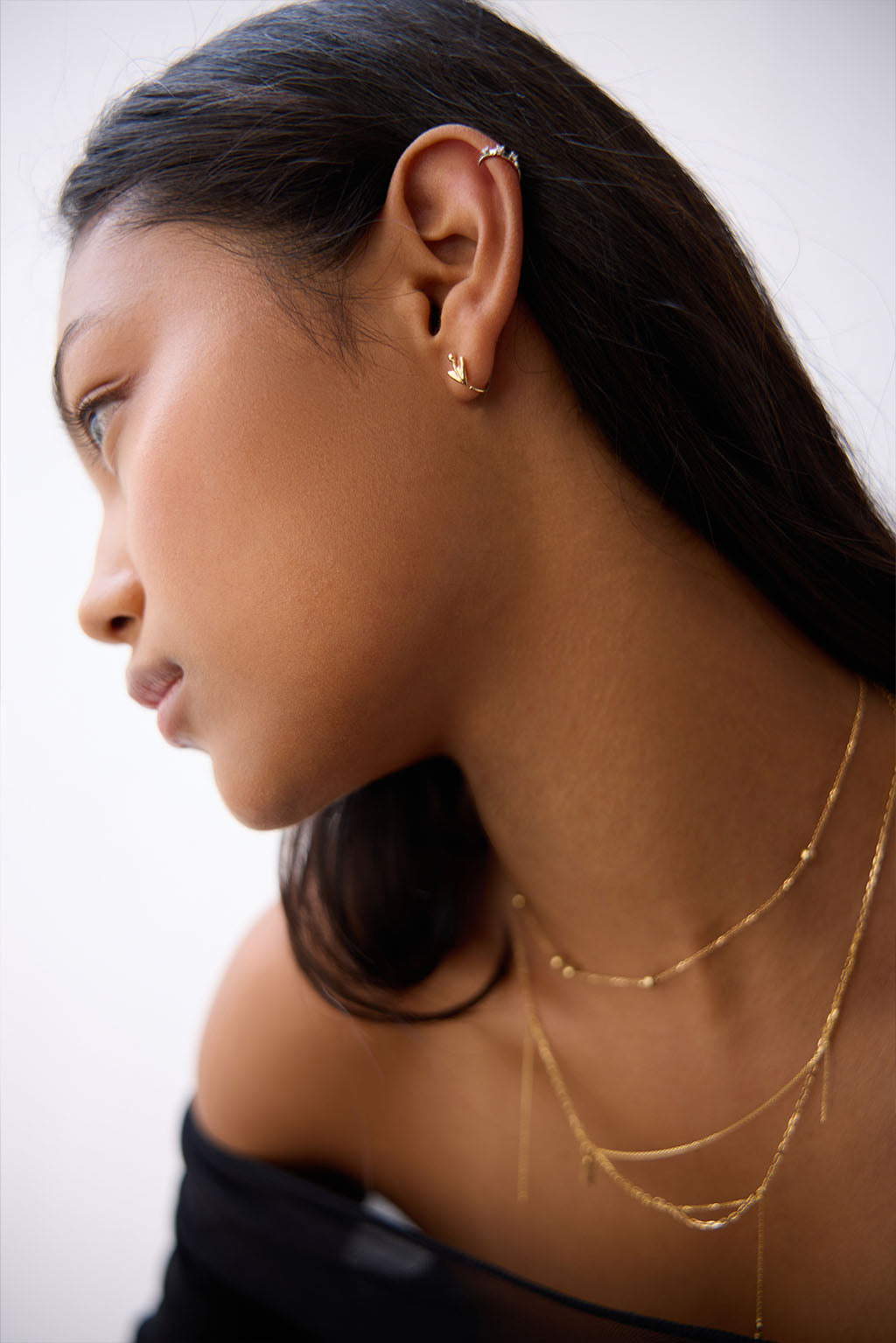 Worn close-up of the Floral Mini Bangle in 18k gold. The sculpted arrow and tiny sphere trace the curve of the ear in a soft, fluid gesture.