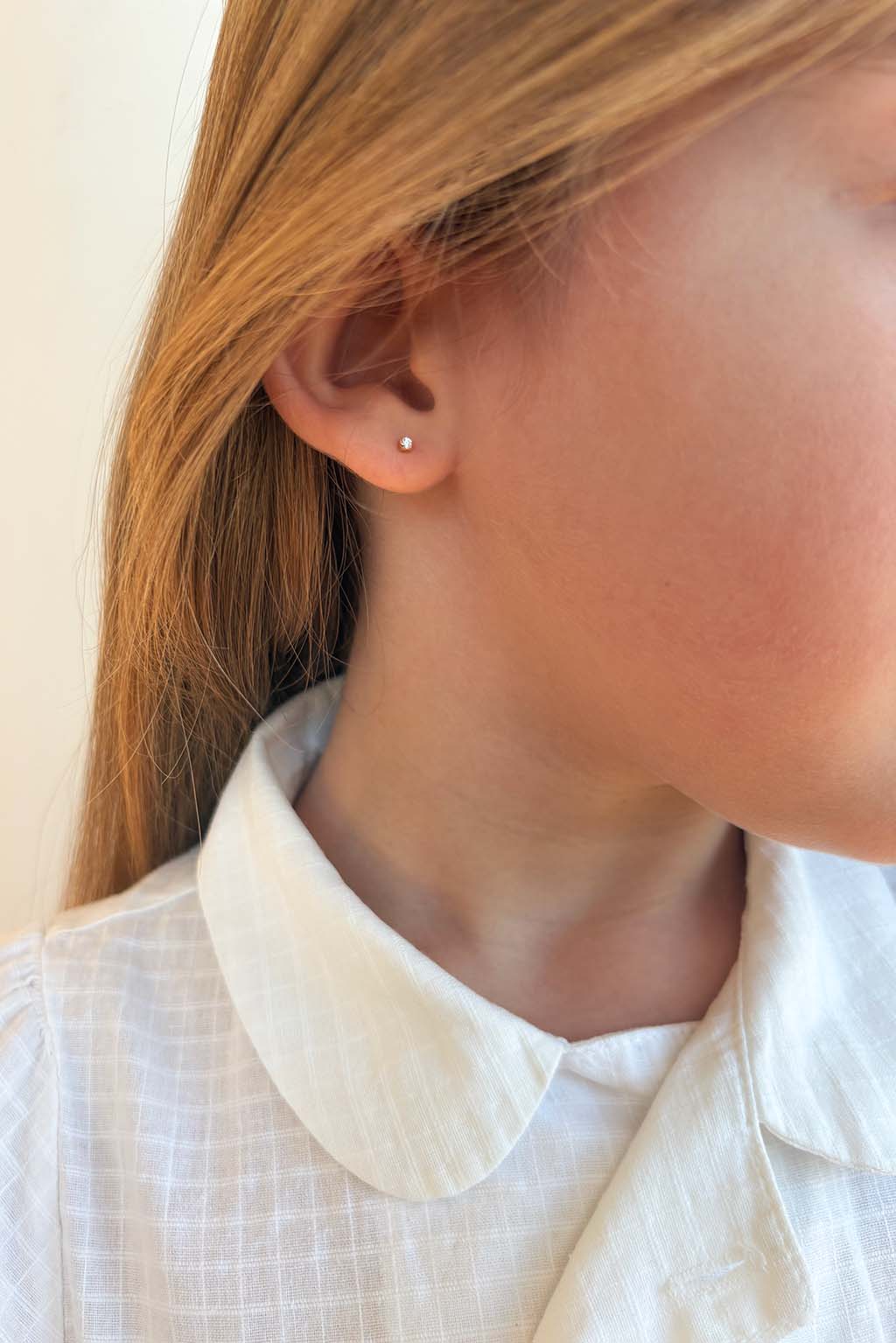 Blond child wearing a single Baby Box 1'7 earring in 18k yellow gold with diamonds by Sansoeurs, visible on one ear.