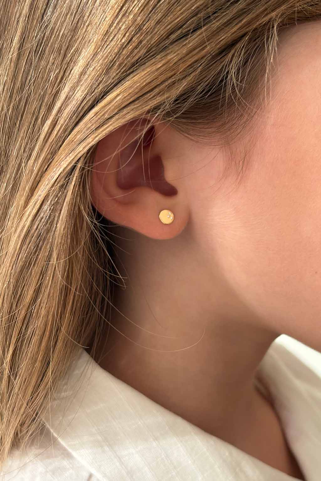 Blond child wearing a single Baby Dots earring in 18k yellow gold with three diamonds by Sansoeurs, visible on one ear.