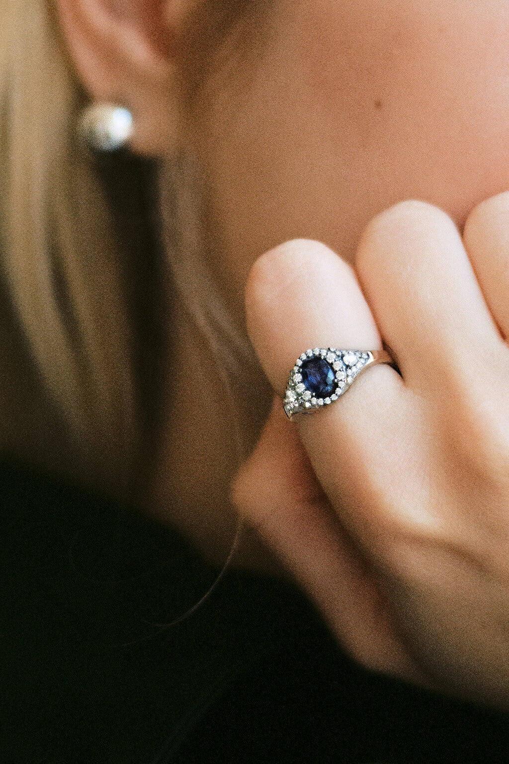 Portrait of a blonde woman showing the Signet Sapphire white 18k gold with diamonds ring in her finger