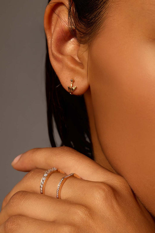 Worn close-up of the Floral Mini Bangle in 18k gold. The sculpted arrow and tiny sphere trace the curve of the ear in a soft, fluid gesture.